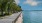 a walkway next to a body of water with trees and a boat in the distance